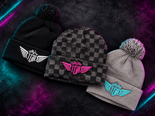 Three TGM beanies with embroidered winged logo: black pom pom, checkered with pink logo, and grey pom pom with teal logo